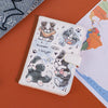 A light pink pu leather passport holder featuring cartoon dogs and text on a wooden surface.