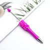 A bright pink glitter ballpoint pen with a silver tip resting on a white paper next to green foliage.