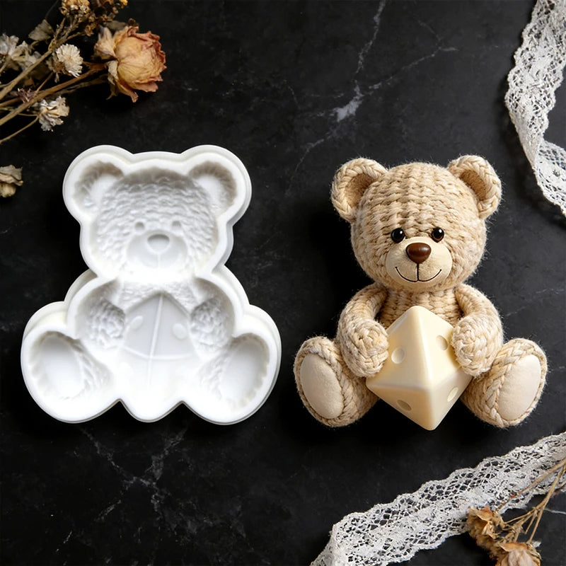 A cream-colored crochet texture teddy bear silicone mold resting on a black surface next to some dried flowers and lace.