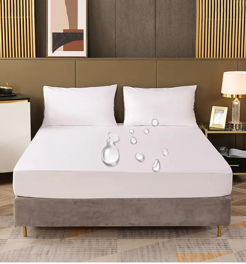 A white fitted mattress protector with an elastic edge resting on a gray upholstered bed base.