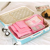 A light blue packing cube set with a lid and multiple pink fabric cubes is displayed on a white bed.