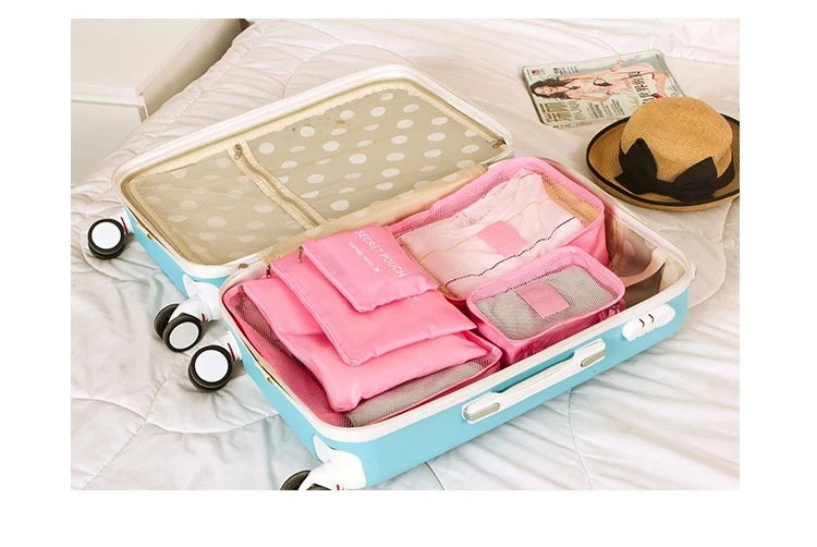 A light blue packing cube set with a lid and multiple pink fabric cubes is displayed on a white bed.