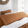 A close-up of a bed with brown linen pillowcases and white sheets.