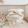 A stack of floral muslin baby blankets and quilts in cream and beige tones are displayed on a light surface.