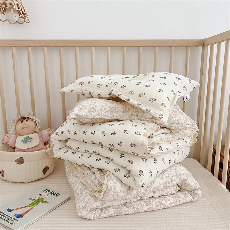 A stack of floral muslin baby blankets and quilts in cream and beige tones are displayed on a light surface.