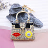 Gold-toned crystal rhinestone handbag keychain with black and gold accents resting on a pink surface.