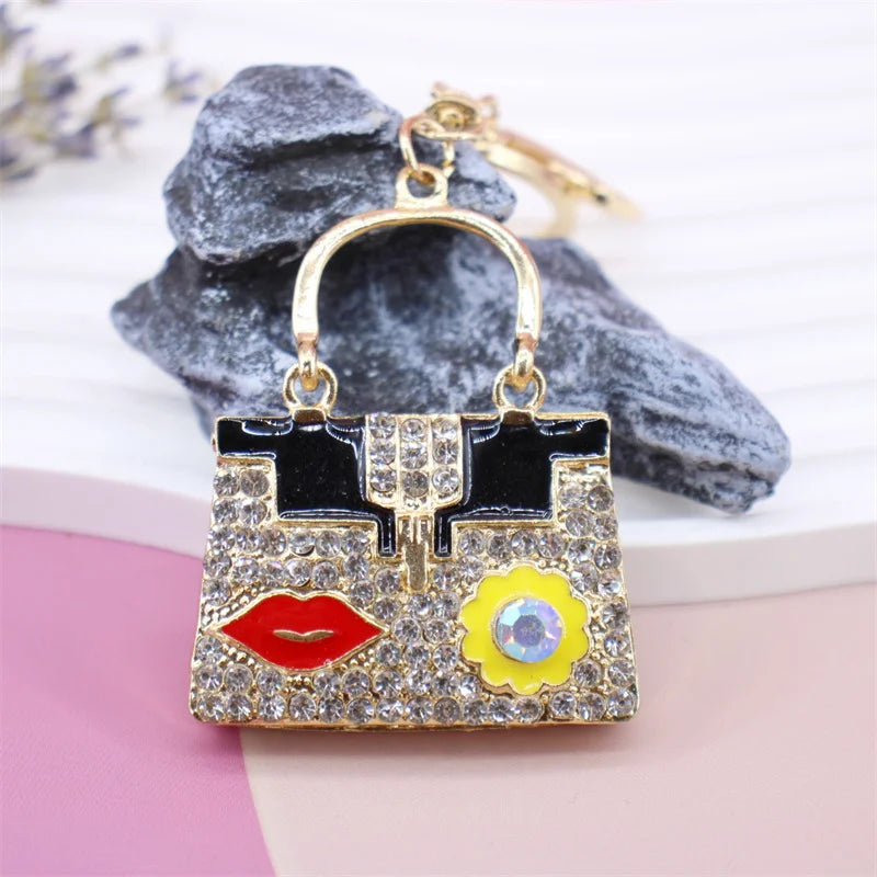 Gold-toned crystal rhinestone handbag keychain with black and gold accents resting on a pink surface.