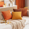A set of three textured corduroy throw pillow covers in shades of orange, mustard yellow, and rust on a light sofa.