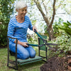An elderly woman sits on a heavy duty foldable garden kneeler seat while using a tool pouch in a garden setting.