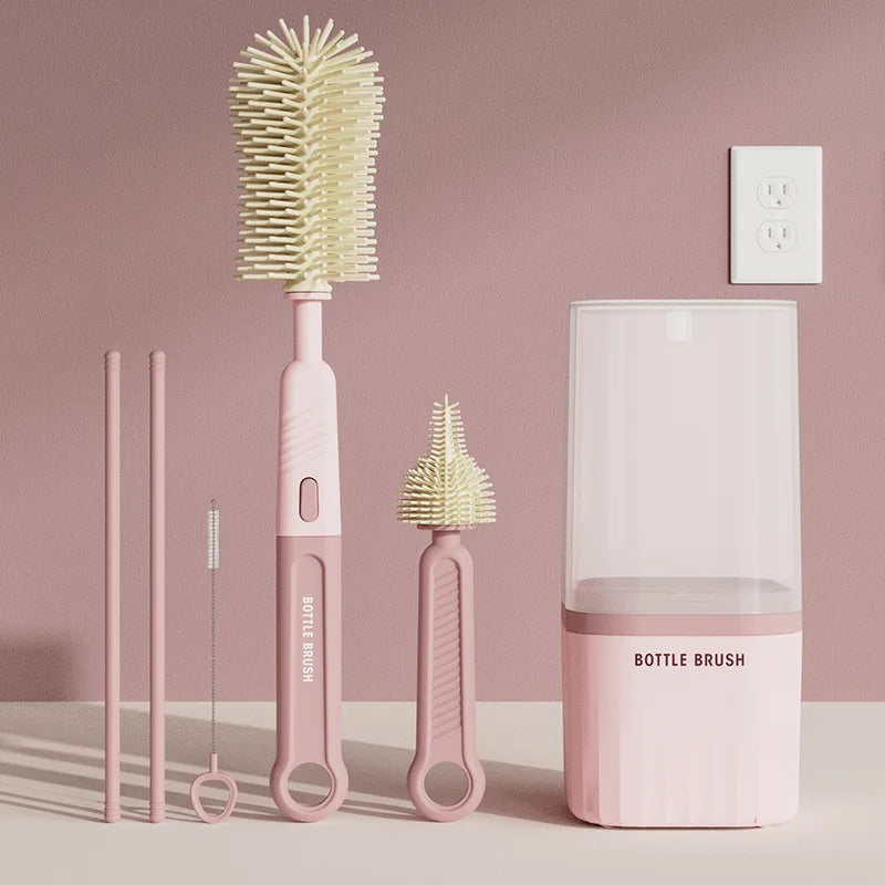 A pink silicone baby bottle brush set with three brushes and a drying rack displayed on a light surface.