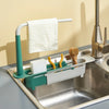 A silver sink features an adjustable sponge holder with a green and white drainer basket and a hanging towel rack.