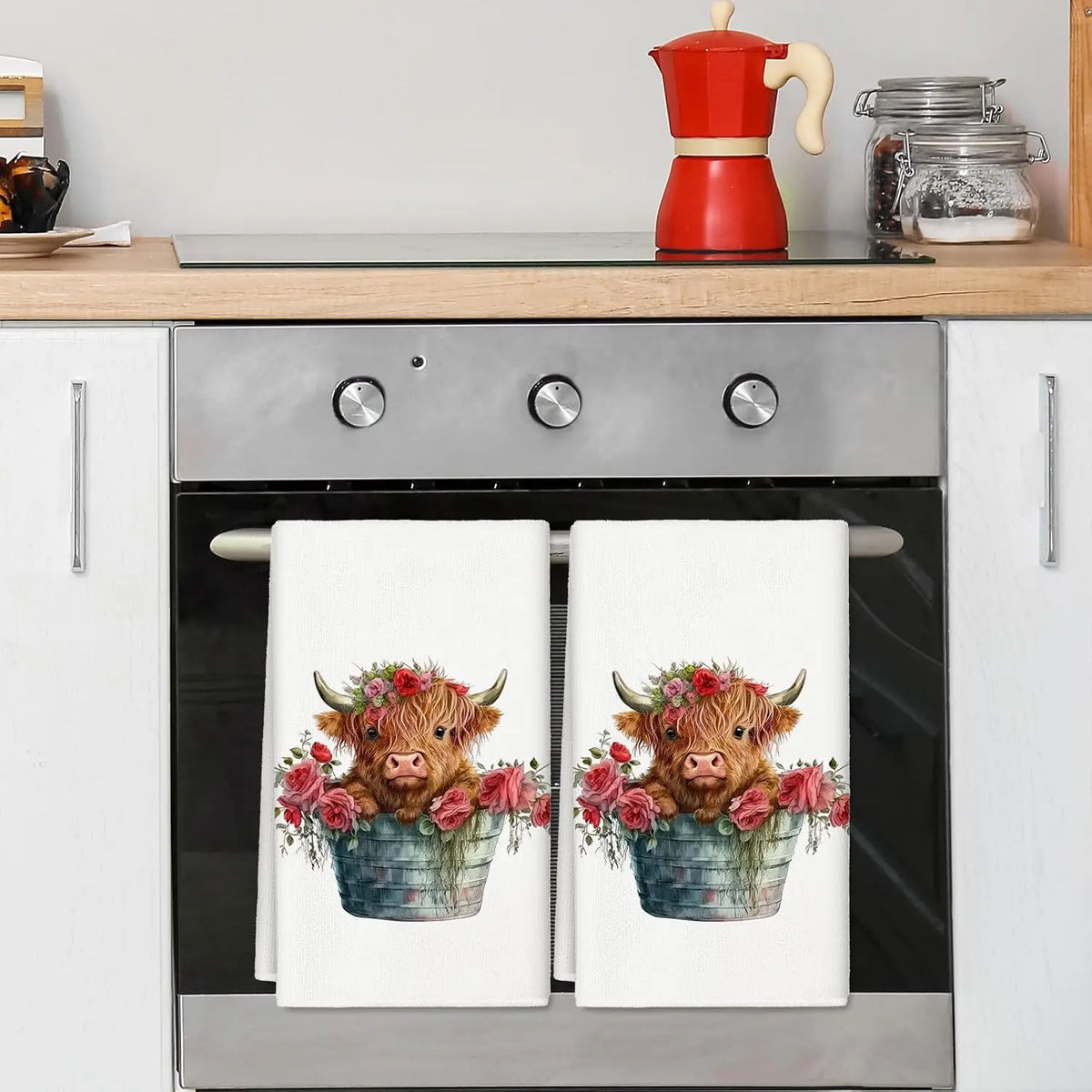 A set of two kitchen towels featuring watercolor illustrations of Highland cows with pink and red flowers.