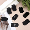 A collection of black aluminum dog tags and blank engraving blanks are displayed on a light background.