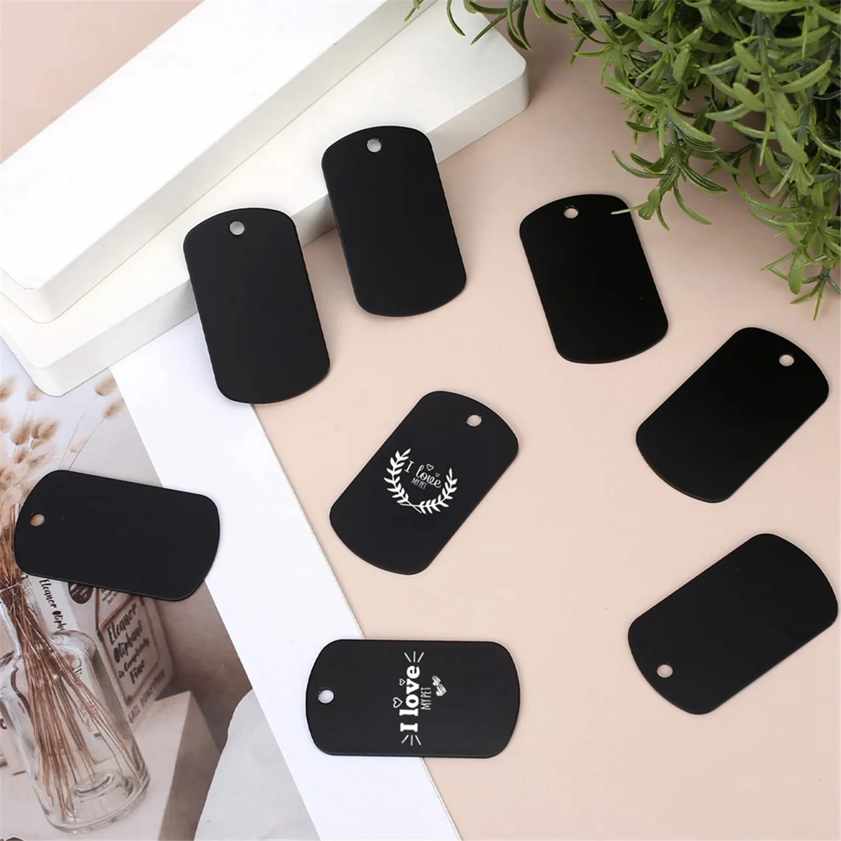 A collection of black aluminum dog tags and blank engraving blanks are displayed on a light background.