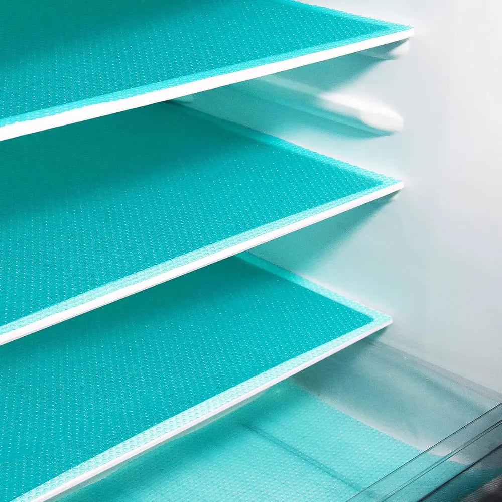A close-up view of a white refrigerator liner mat with teal mesh inserts inside a storage shelf.