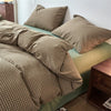 A plaid duvet cover in olive green and brown tones with matching pillows on a bed.