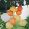 A collection of round paper lanterns in white, orange, and yellow hanging outdoors.