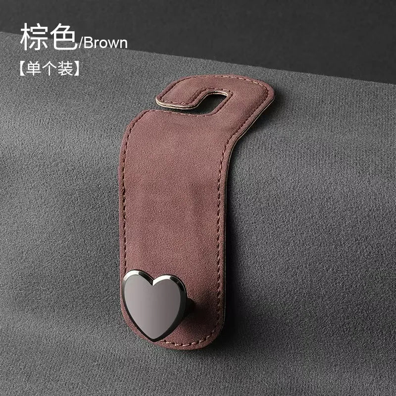 A brown car seat headrest hook with a heart-shaped silicone grip is shown against a dark gray background.