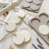 A collection of white silicone discs for hanging soap and aromatherapy, displayed on a linen fabric.