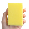 A hand holds a bright yellow double-sided kitchen scouring pad with a nano emery surface.