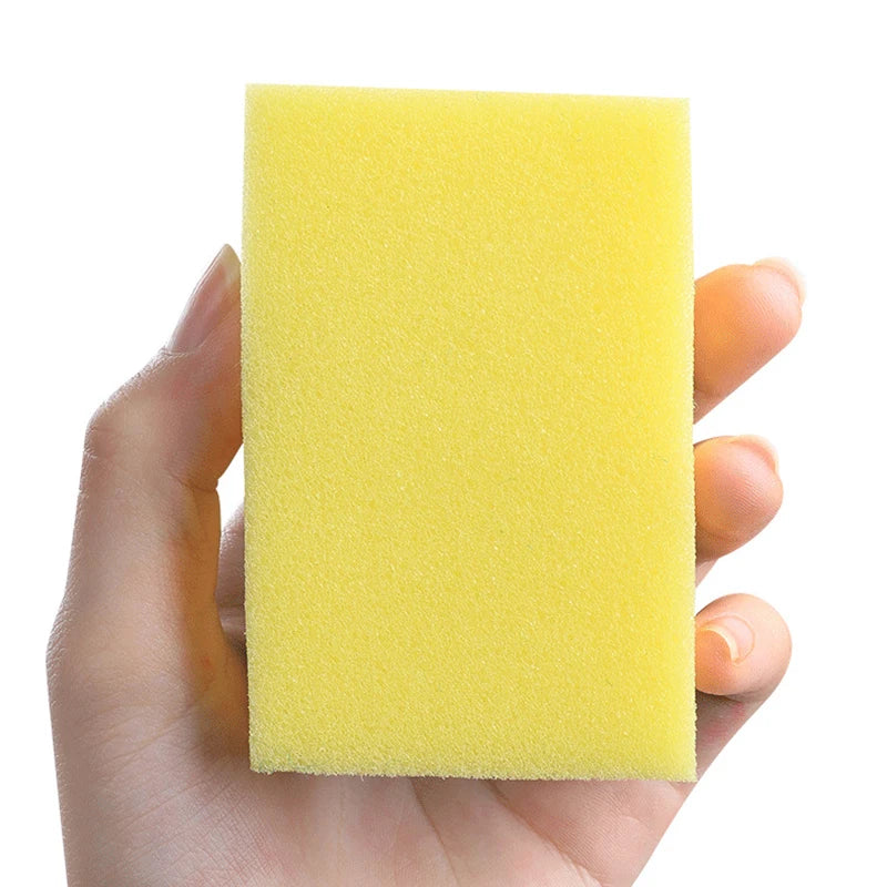 A hand holds a bright yellow double-sided kitchen scouring pad with a nano emery surface.