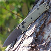 A folding pocket knife with a drop point blade is shown resting on a tree trunk.
