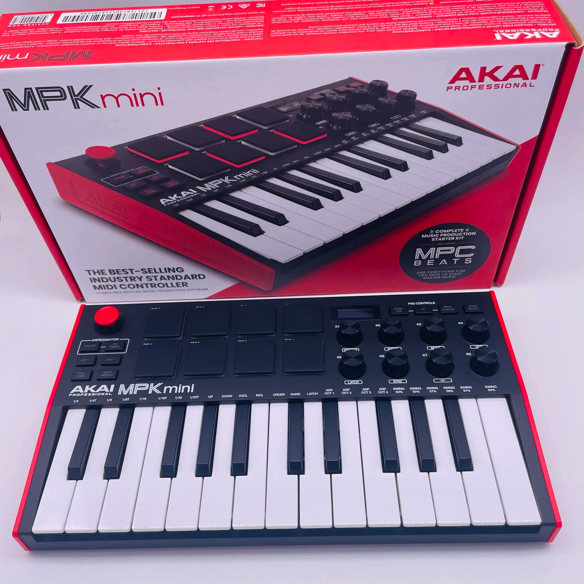 A red box and a white MIDI keyboard controller featuring drum pads and knobs for the AKAI MPK Mini.