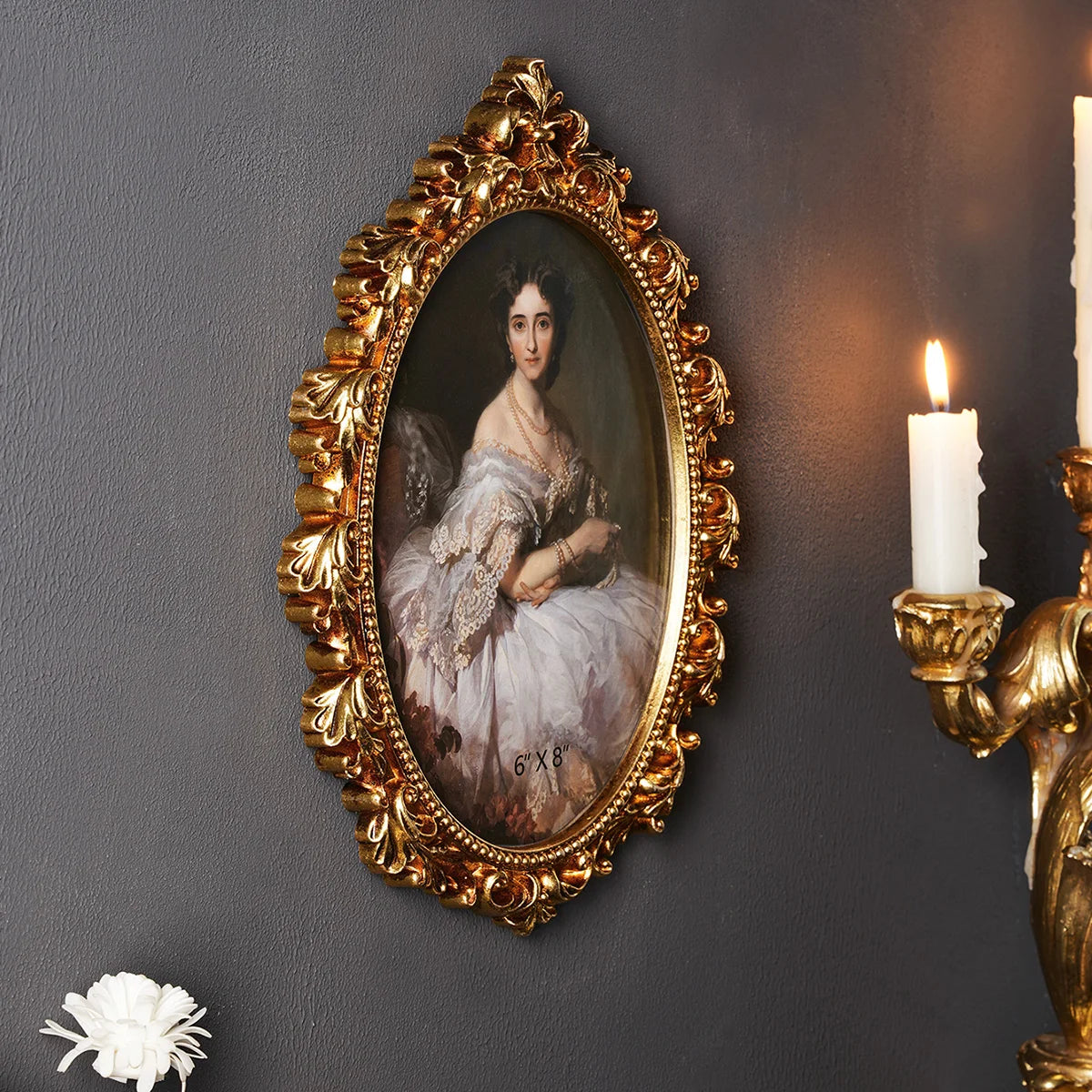 An ornate gold-framed oil painting of a woman against a dark gray wall with a lit candle nearby.