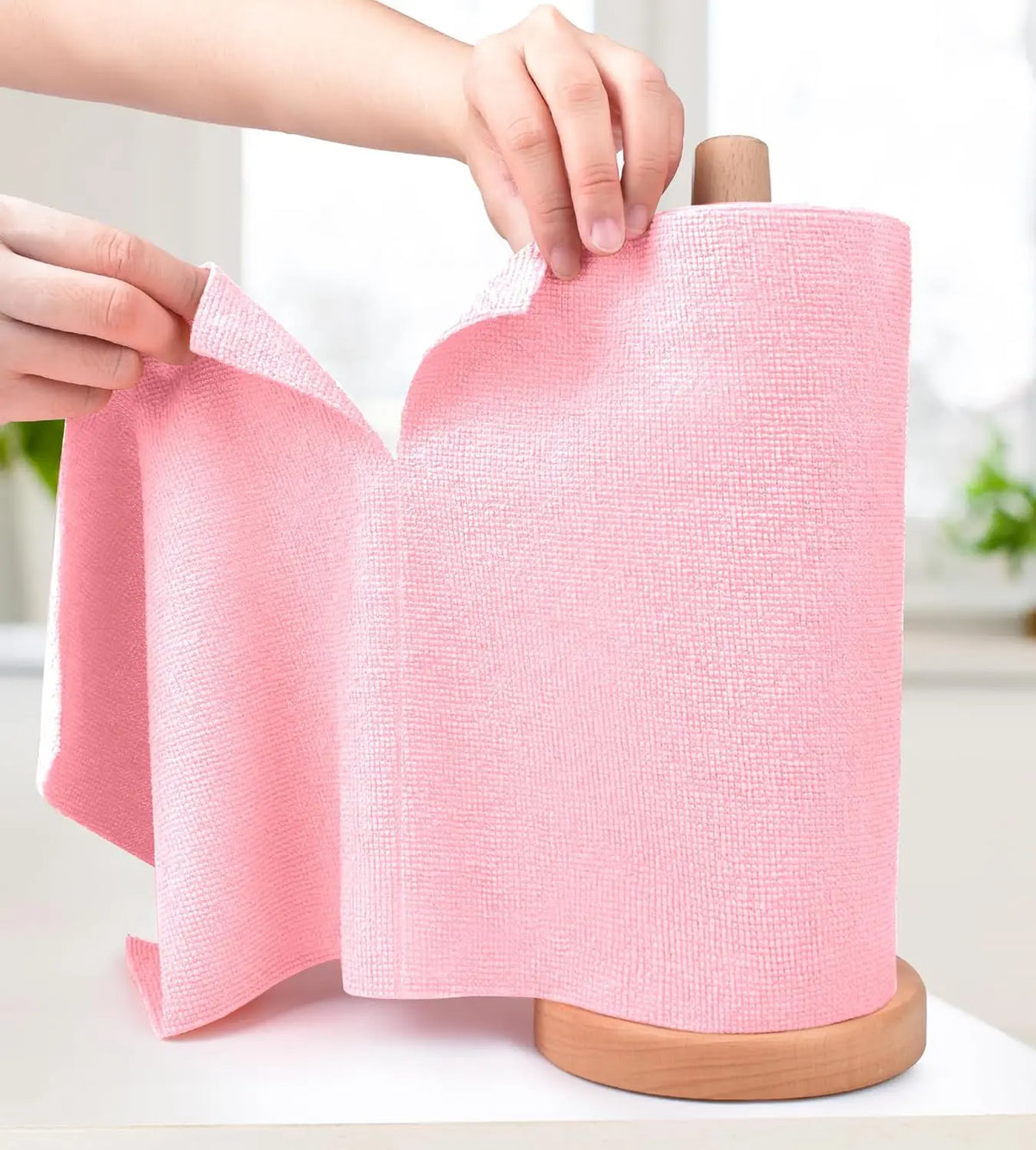A hand is holding a pink reusable microfiber cleaning cloth rolled on a wooden spindle.