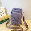 A purple bow-decorated casual crossbody bag with an adjustable strap resting on a light surface.