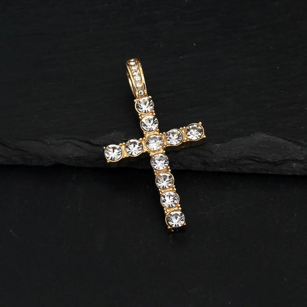 Pendentif en forme de croix doré avec des pierres claires sur une chaîne de tennis, présenté sur une surface noire.