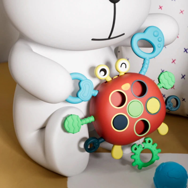 A white silicone pull string sensory toy for babies with colorful rings and textures.