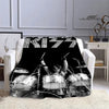 A black flannel throw blanket featuring a graphic print of the KISS band logo and members on a white sofa.