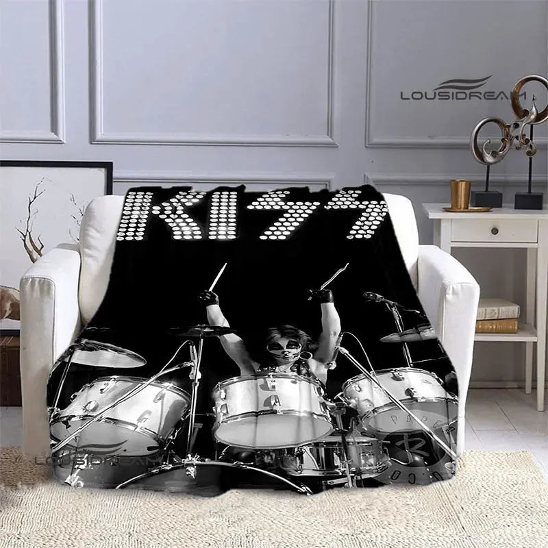 A black flannel throw blanket featuring a graphic print of the KISS band logo and members on a white sofa.