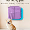 A purple silicone pet licking pad is shown next to a small dog, with a blue version visible on the floor.