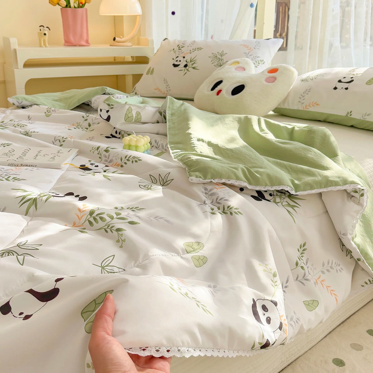 A white comforter with a panda print featuring green and orange foliage, displayed on a bed.