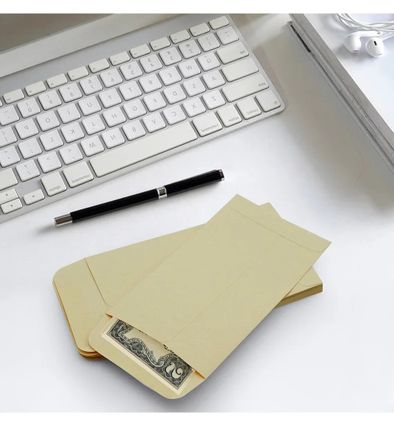 A set of kraft paper cash envelopes is shown next to a white keyboard and a black pen on a white desk.