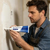 A man applies wall repair paste to a textured wall surface using a squeeze bottle.