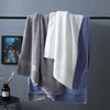A stack of gray and white bath towels hanging on a black rack against a gray wall.