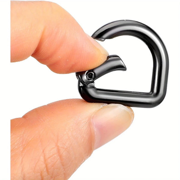 A hand is holding a black stainless steel D-ring clip with a snap hook for bags or keychains.