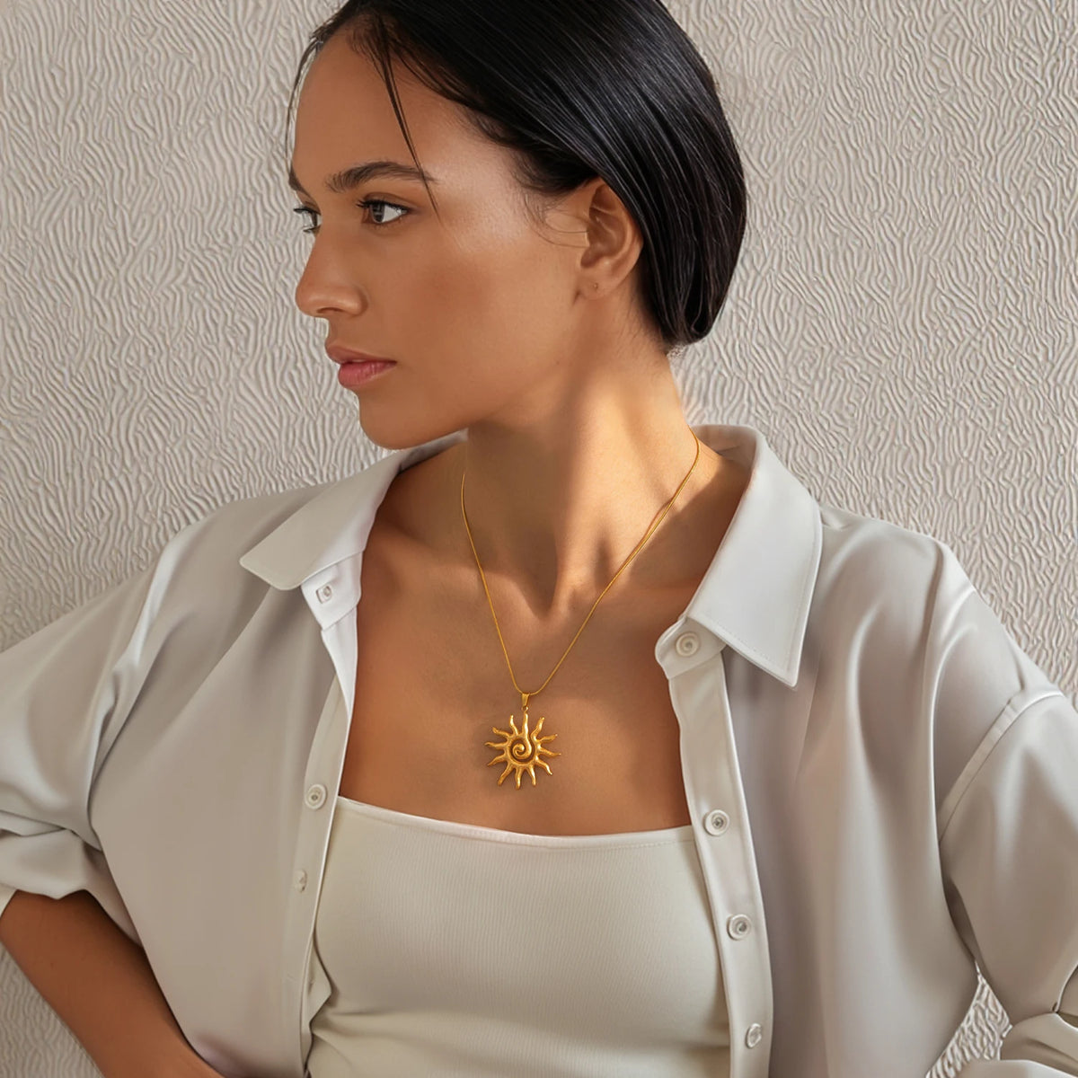 Eine Frau trägt eine goldene Spiral-Sonne-Kette unter einem weißen Hemd.
