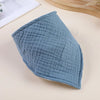 A light blue, textured cotton baby bib is shown angled on a beige surface.