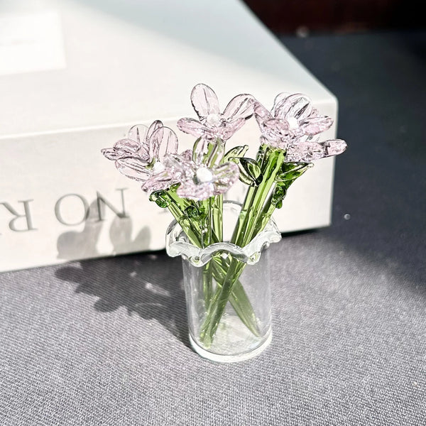 A small glass vase holds a bouquet of pink eternal flowers on a gray surface.