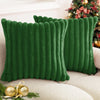 A deep emerald green plush faux fur square cushion cover with vertical stripe detailing resting on a light sofa.