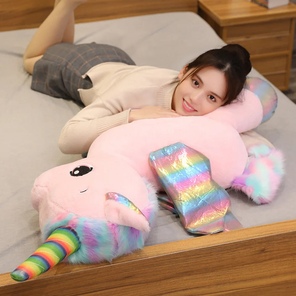 A woman is relaxing on a bed with a pink unicorn plush toy and a rainbow-colored accessory.