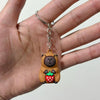 A small keychain charm shaped like a brown capybara holding a red strawberry, attached to a silver ring.