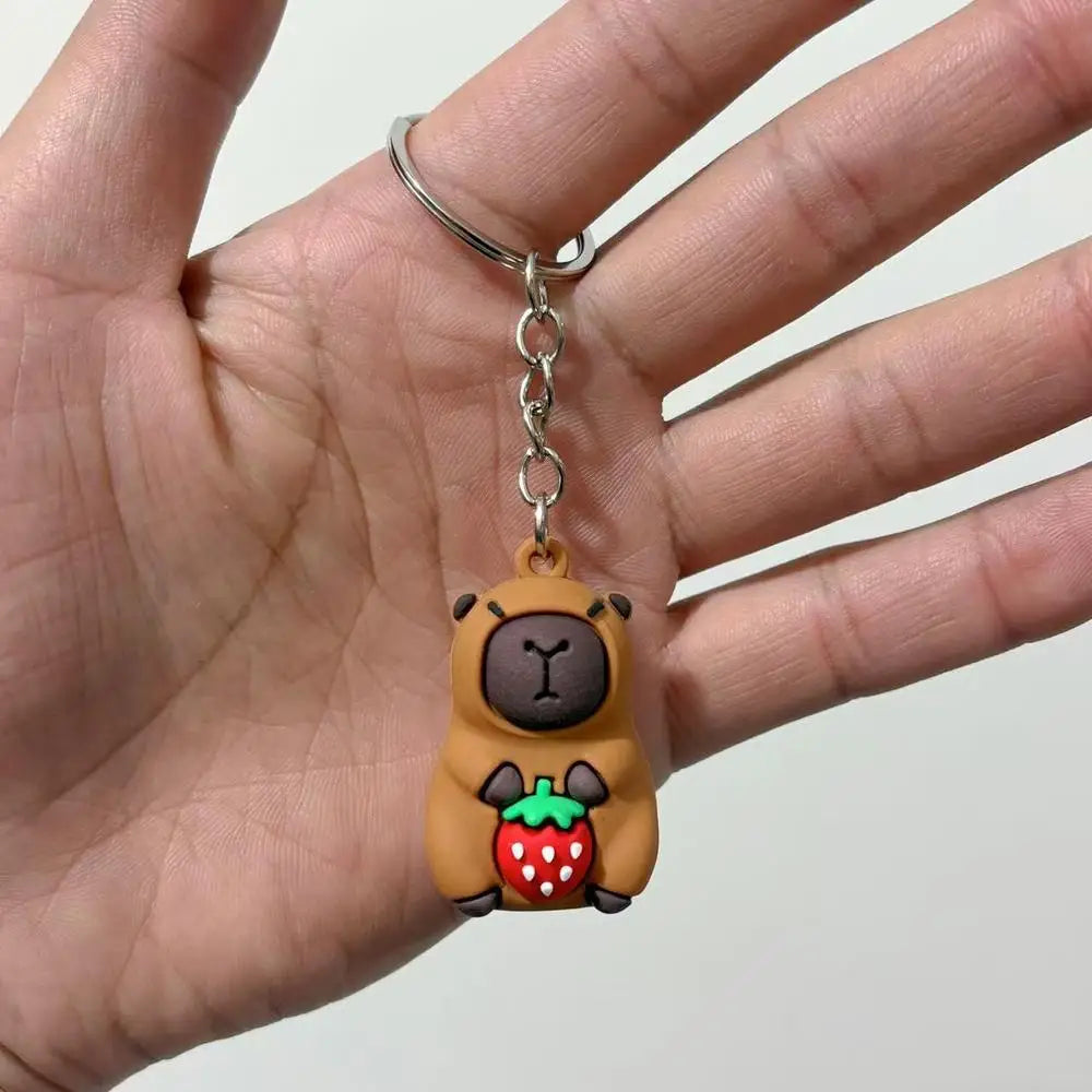 A small keychain charm shaped like a brown capybara holding a red strawberry, attached to a silver ring.
