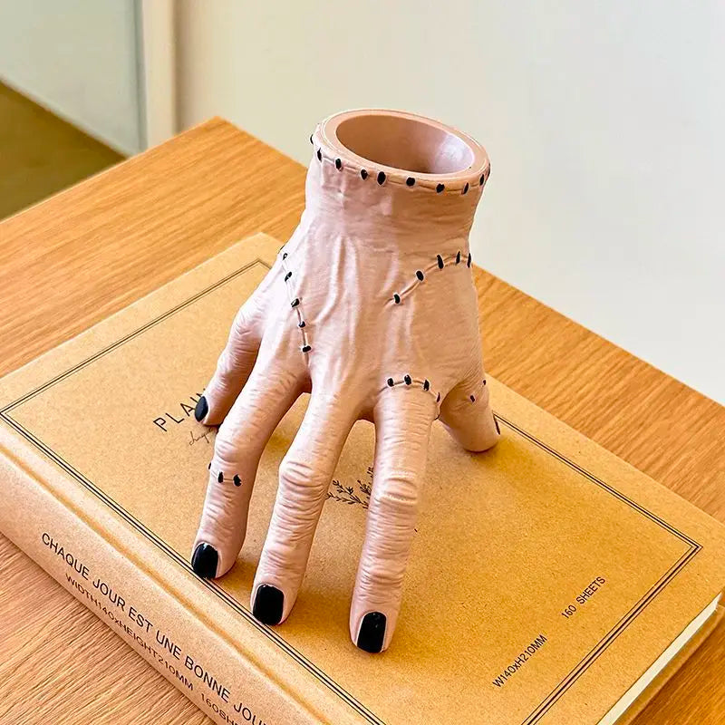 A light pink resin hand planter and pen holder resting on a brown book.