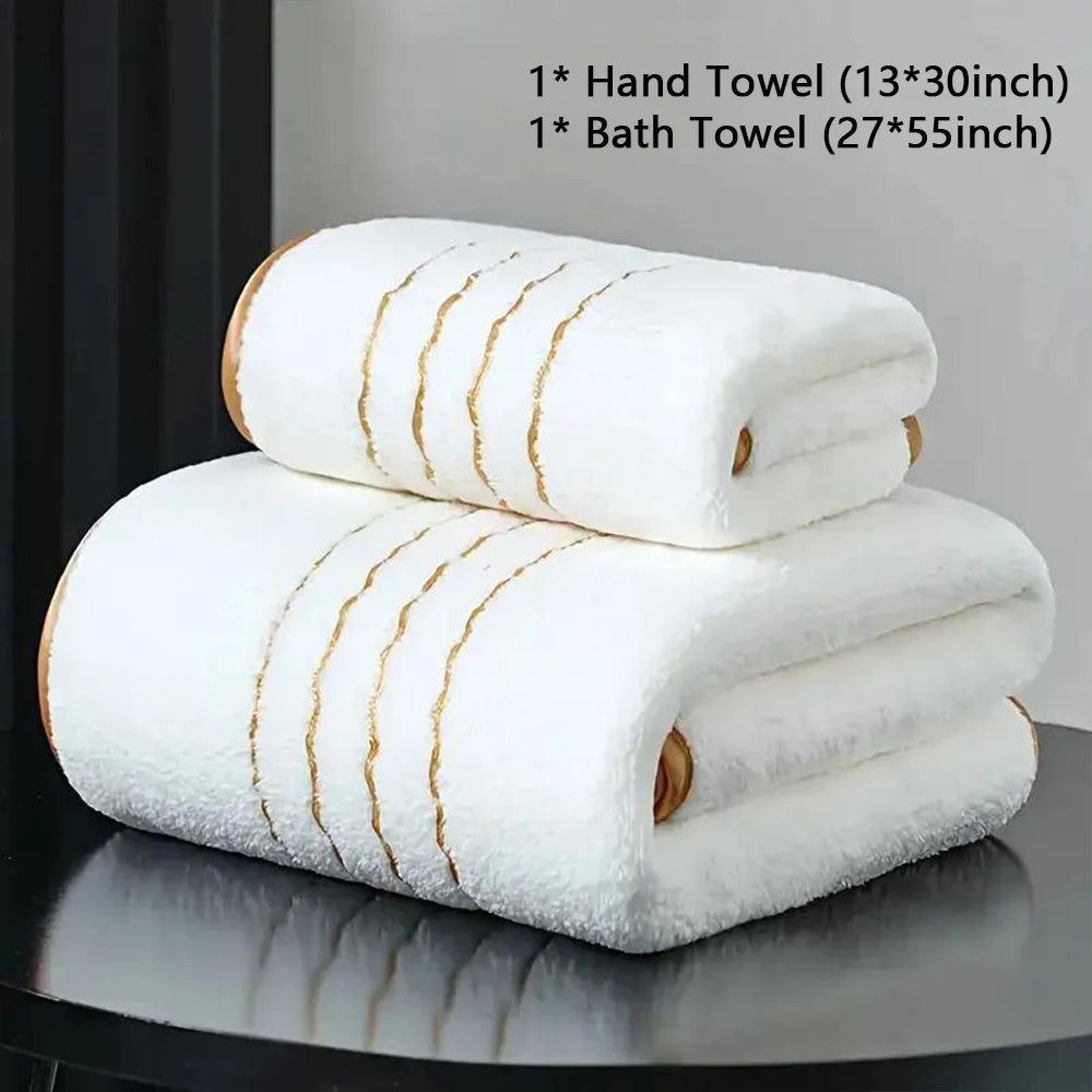 A stack of white bath and hand towels with gold stripes displayed on a dark surface.