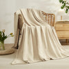 A beige soft muslin cotton blanket draped over a wicker chair in a bright, natural setting.